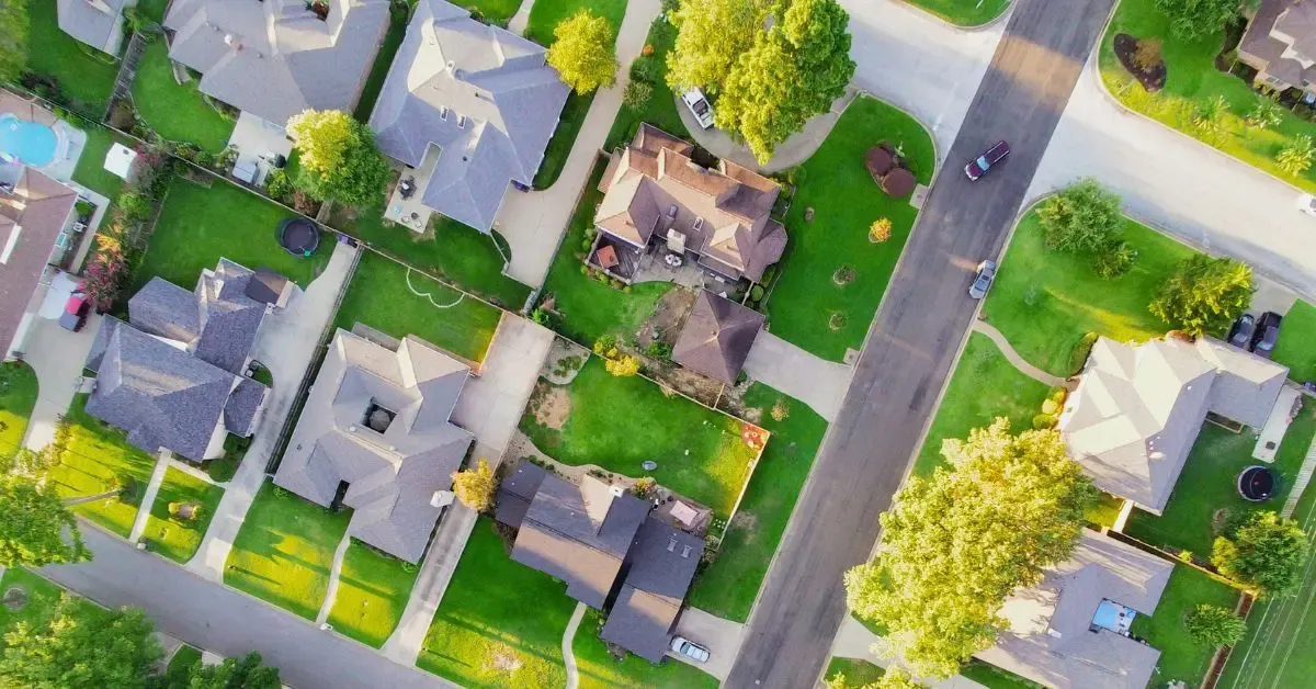 Aerial view of a suburban neighborhood: grey-roofed houses, green lawns and a car driving down the street