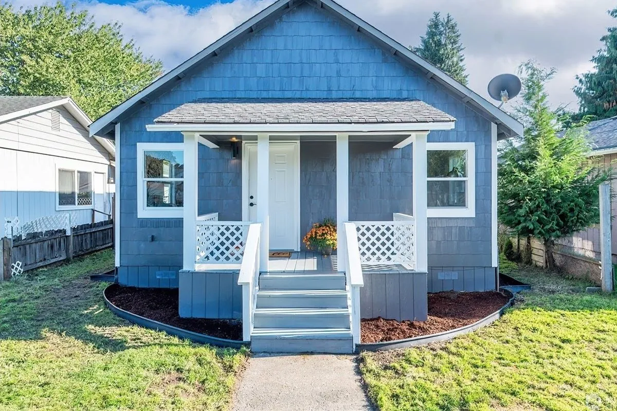 The same Longview, WA house after work: new blue shingle siding, a rebuilt white porch and rail, new steps and fresh landscaping