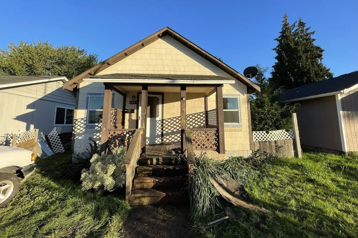 The Longview, WA house before work: faded paint, a bare wooden porch and broken, rotting front steps