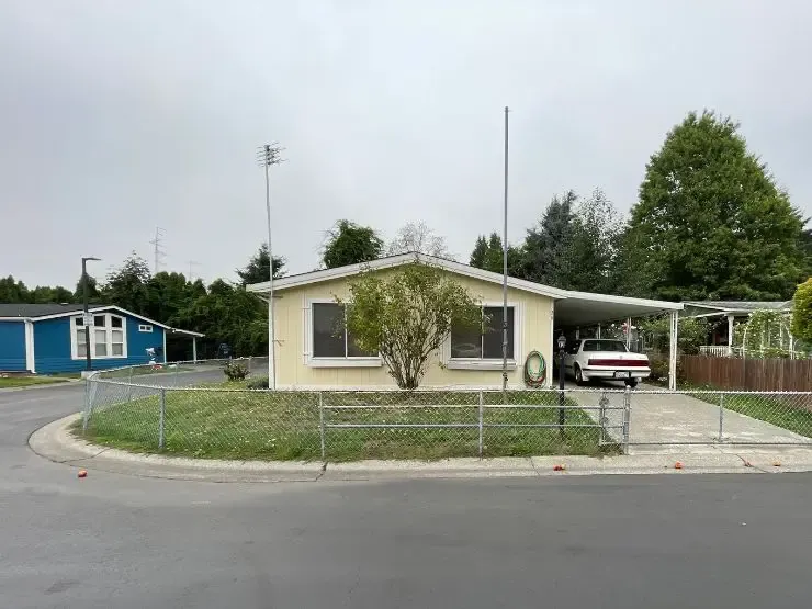 A cream manufactured home with a carport and a chain-link fenced lawn