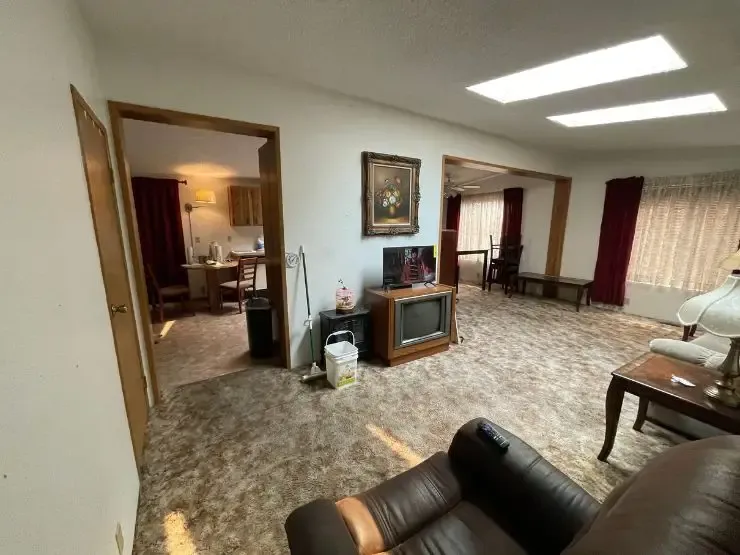 The living room of an inherited house, still furnished, with worn carpet and an old television left where it stood
