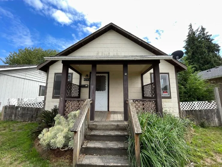 A small cream bungalow with a covered porch and weathered wooden steps