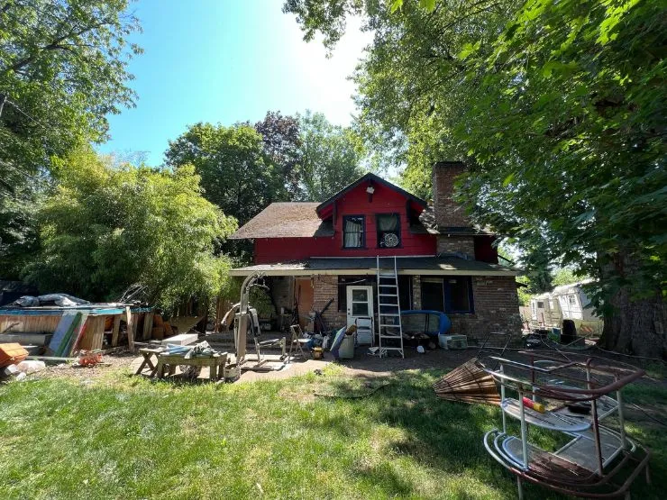 A weatherboard house with peeling paint, a sagging porch roof and a yard full of stored belongings